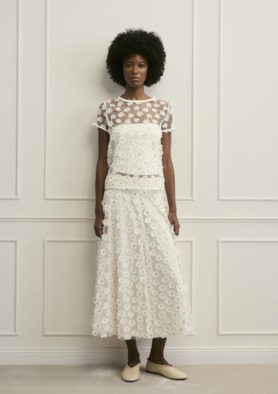 Model trägt Oberteil und Rock mit Gänseblümchen Ornamenten der Marke Luisa Cerano.