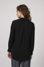 Model zeigt eine schwarze Bluse mit Strass-Dekor am Kragen der Marke Janice & Jo, eine mittelgraue Stoffhose der Marke Cambio und einen Gürtel der Marke Dorothee Schumacher.