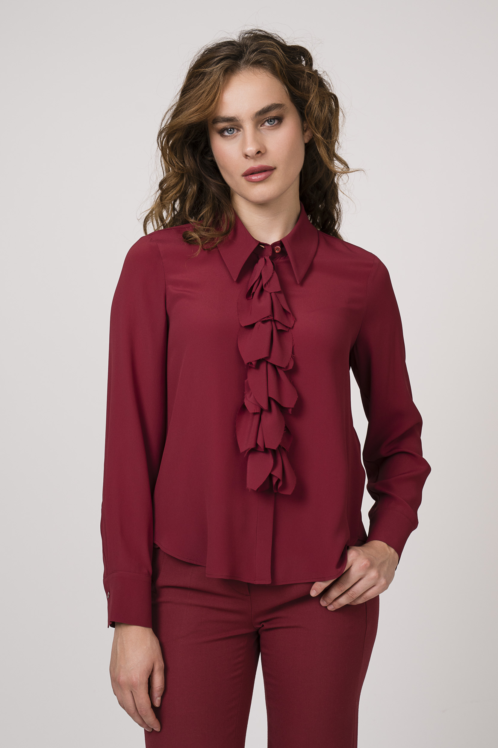 Model zeigt ein Outfit der Marke Luisa Cerano bestehend aus einer bordeaux-roten Bluse mit Vollant und einer bordeaux-roten Hose.