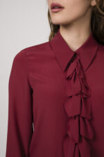 Model zeigt ein Outfit der Marke Luisa Cerano bestehend aus einer bordeaux-roten Bluse mit Vollant.