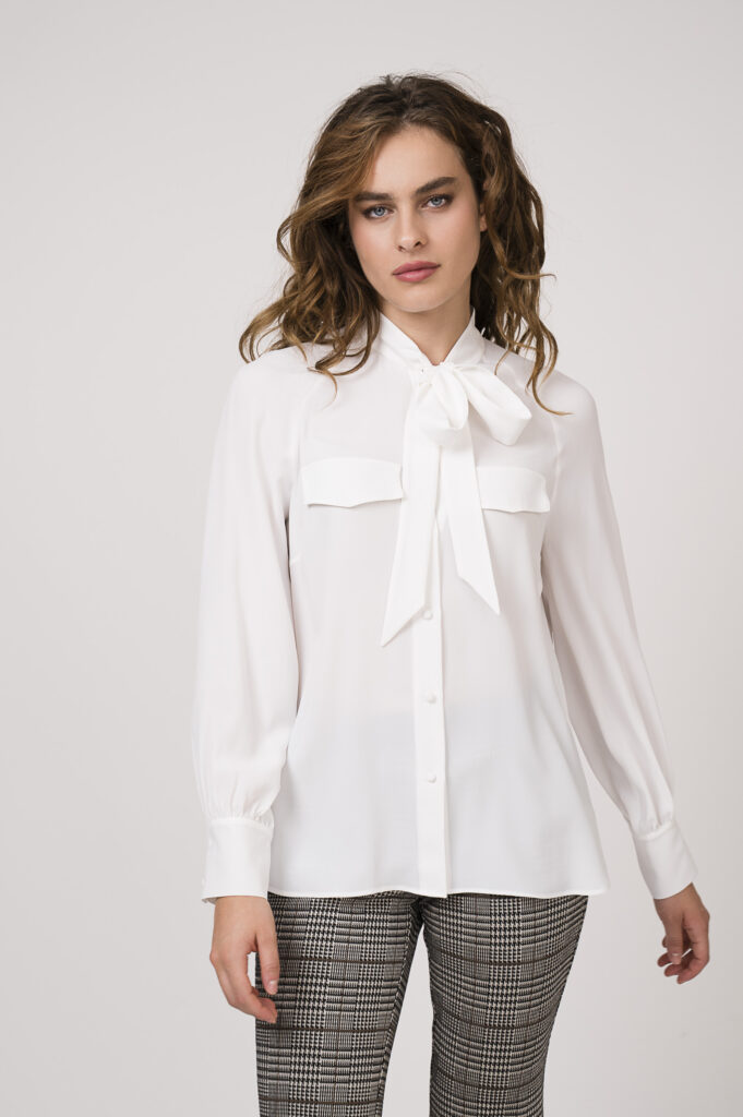 Model zeigt eine weiße Bluse mit Schleife der Marke Luisa Cerano und eine karierte Stoffhose der Marke Cambio.