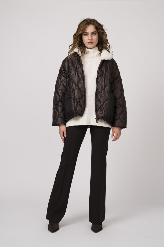 Model zeigt einen natur-farbigen Stehkragenpullover der Marke Dorothee Schumacher, eine braue Stoffhose der Marke Dorothee Schumacher und eine braune Steppjacke der Marke Dorothee Schumacher.