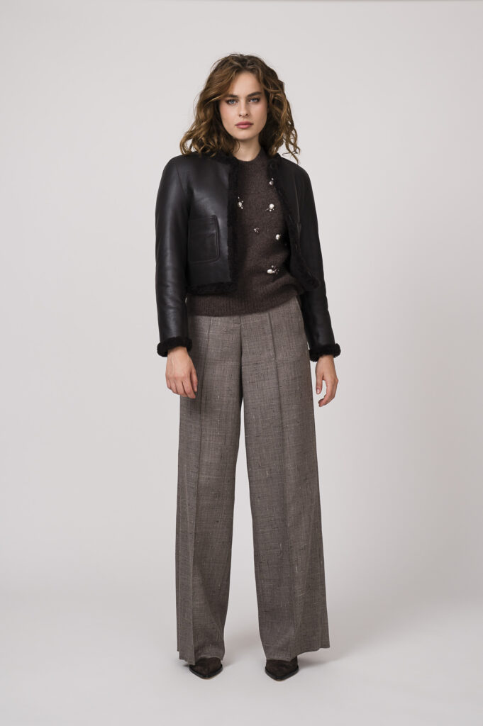 Model zeigt einen braunen Pullover mit Perlendekor der Marke Dorothee Schumacher, eine braue Stoffhose der Marke Dorothee Schumacher und eine Wendejacke der Marke Dorothee Schumacher.