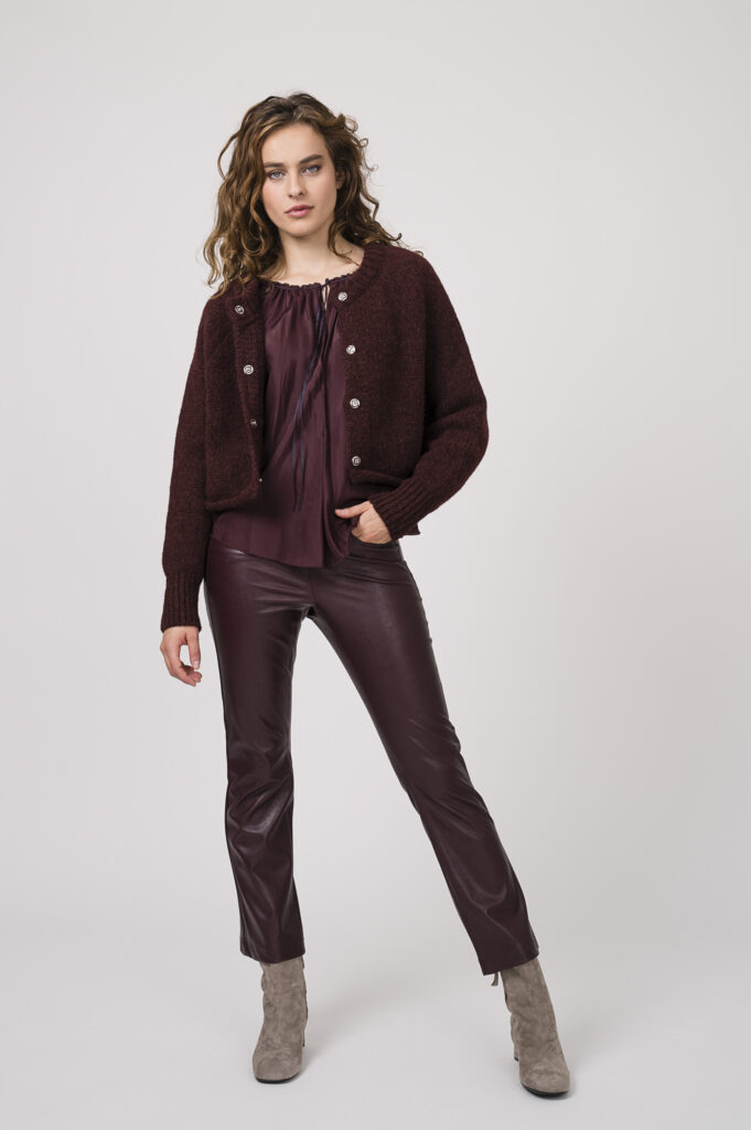 Model zeigt ein Outfit der Marke Susanne Bommer - bestehend aus einer bordeaux-roten Strickweste, einem langärmligen bordeaux-roten Seidenshirt, einer bordeaux-roten Hose der Marke Cambio.