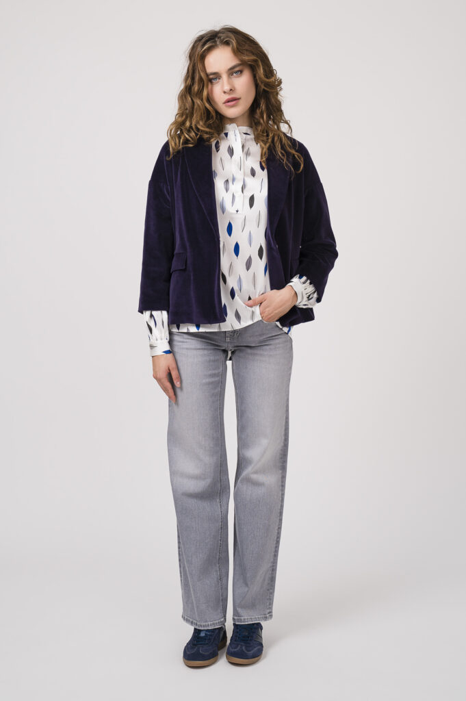 Model zeigt eine gemusterte Bluse der Marke Herzens'Angelgenheit, eine Jeans der Marke Cambio, einen violetten Blazer der Marke Circolo und blaue Sneaker der Marke Caval.