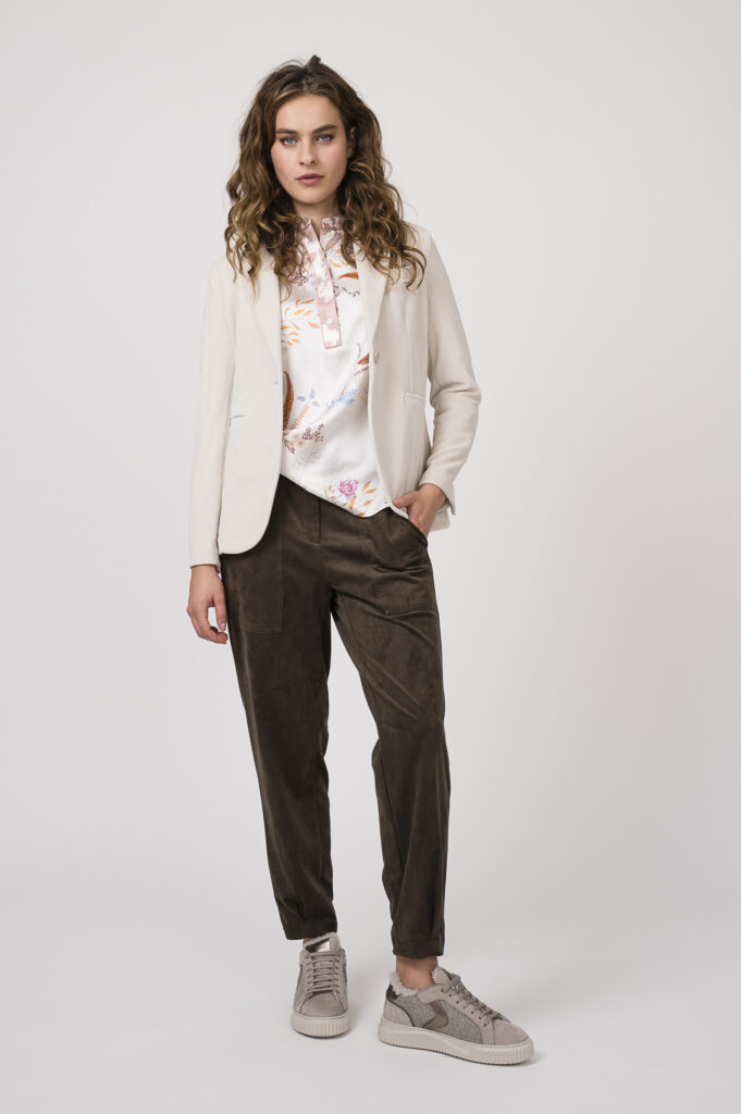 Model zeigt einen natur-farbigen Blazer der Marke Circolo, eine Bluse der Marke Herzens'Angelegenheit, eine schoko-braune Stoffhose der Marke Cambio und Sneaker der Marke Voile Blanche.