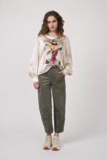 Model zeigt eine beige gemusterte Bluse der Marke Grace, eine olivgrüne Hose der Marke Cambio und Speaker der Marke Voile Blanche.