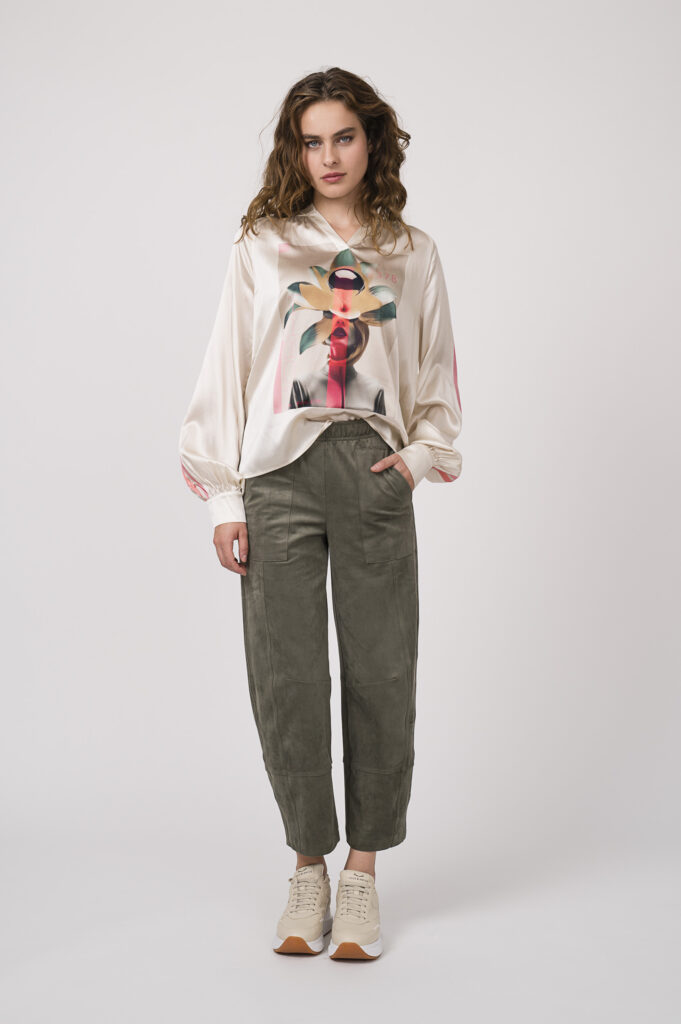 Model zeigt eine beige gemusterte Bluse der Marke Grace, eine olivgrüne Hose der Marke Cambio und Speaker der Marke Voile Blanche.
