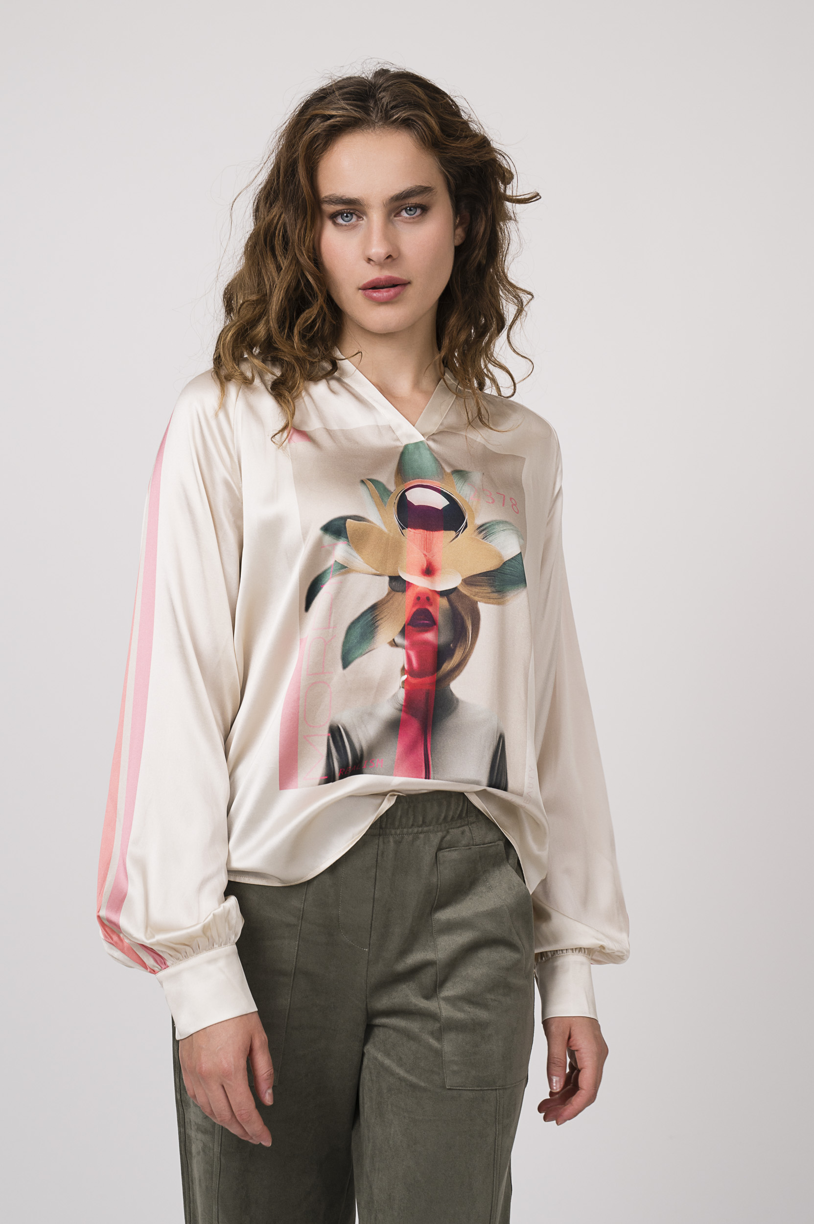 Model zeigt eine beige gemusterte Bluse der Marke Grace, eine olivgrüne Hose der Marke Cambio.
