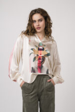 Model zeigt eine beige gemusterte Bluse der Marke Grace, eine olivgrüne Hose der Marke Cambio.