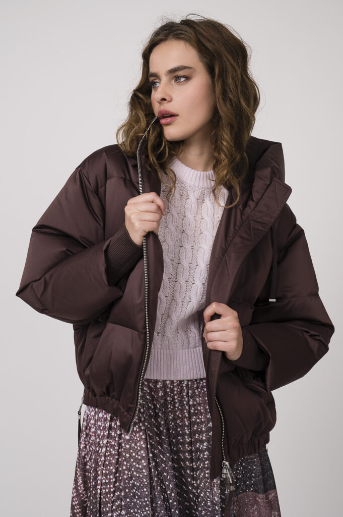 Model zeigt eine bordeaux-rote Daunenjacke von DUNO, einen Kurzarmpullover in rose der Marke Dorothee Schumacher und einen bordeaux-rot gemusterten Rock der Marke Talking Walls.