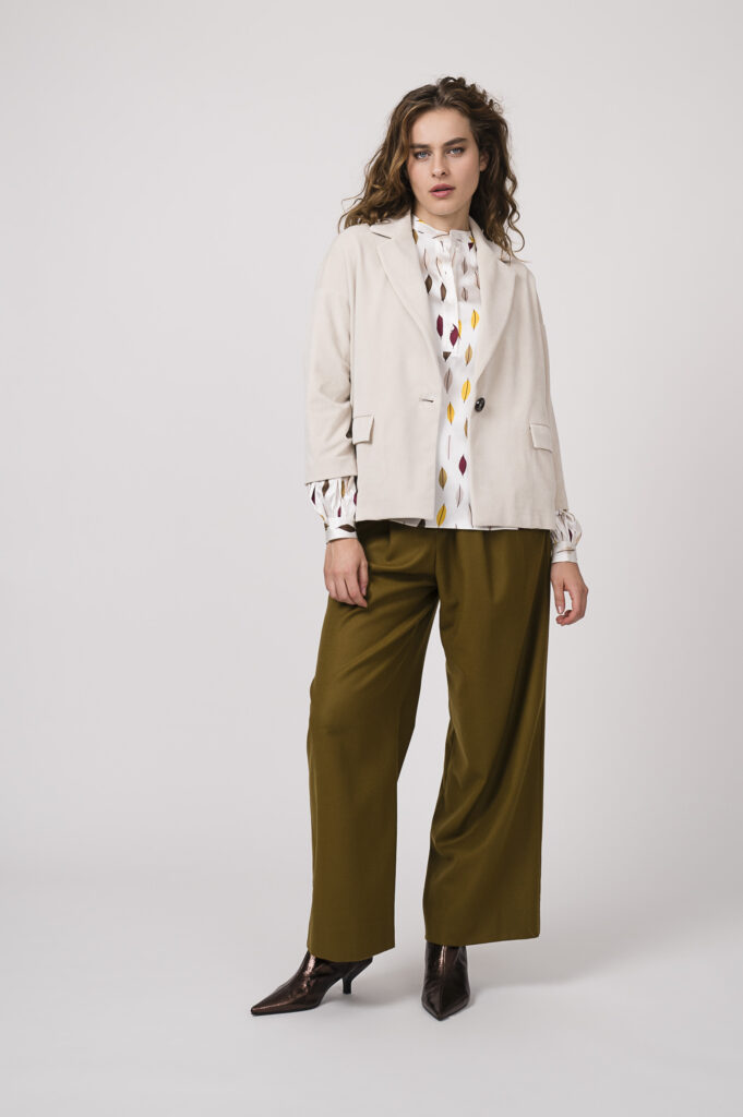 Model zeigt eine natur-farbige Blazerjacke von Circolo, eine gemusterte Bluse der Marke Herzens’Angelegenheit und eine curry-farbige Stoffhose der Marke Susanne Bommer.