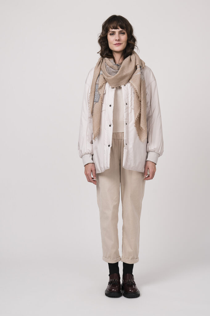 Model zeigt eine Steppjacke der Marke Lis Lareida in natur, dazu einen Kurzarmpullover der Marke Allude in natur aus cashmere und eine Cordhose der Marke Lis Lareida in sand, Schal der Marke Hemisphere