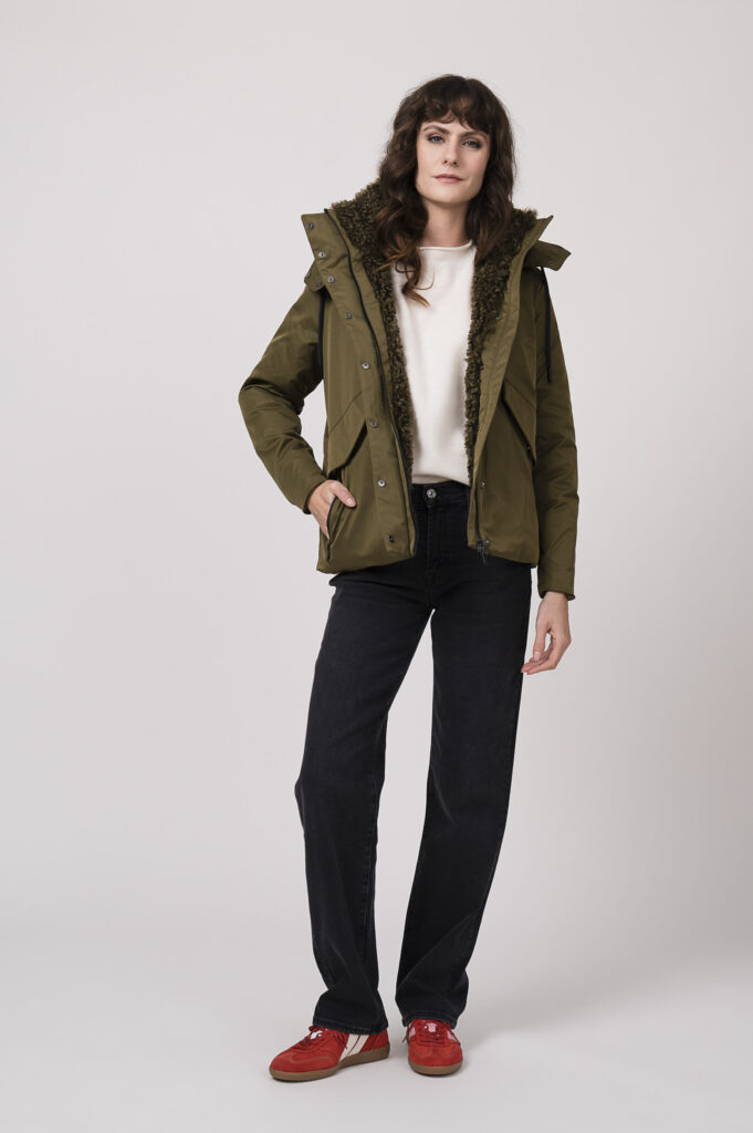 Model zeigt eine Steppjacke der Marke Save the Durck in olive, einen Pullover der Marke FFC in winterweiß, dazu eine Jeans der Marke 7 for all mankind und Sneaker der Marke Caval in rot