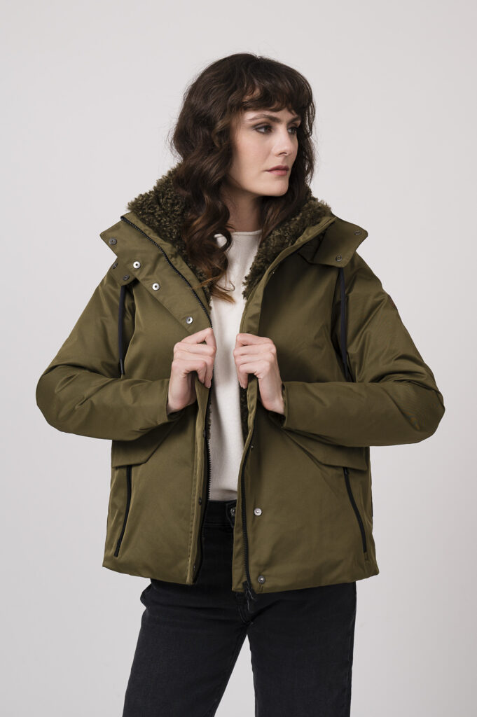 Model zeigt eine Steppjacke der Marke Save the Durck in olive, einen Pullover der Marke FFC in winterweiß, dazu eine Jeans der Marke 7 for all mankind und Sneaker der Marke Caval in rot