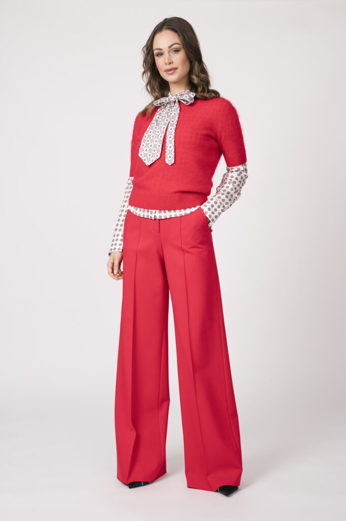 Model trägt einen roten Kurzarmpullover, eine weiß gemusterte Bluse und eine rote Stoffhose der Marke Dorothee Schumacher.