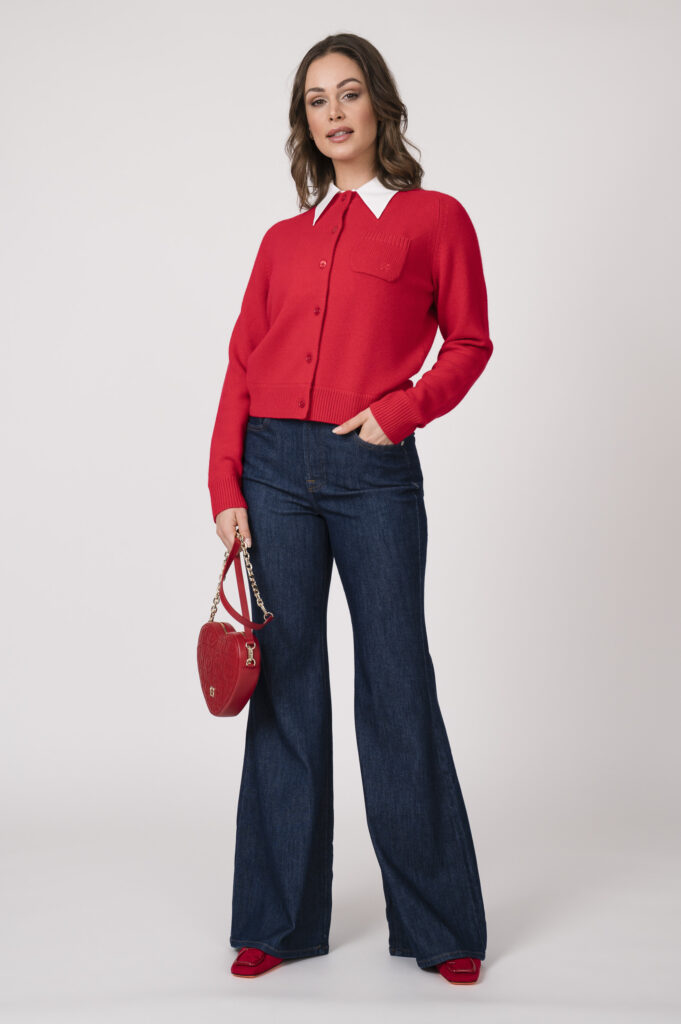 Model trägt einen roten Strickweste mit weißem Blusenkragen der Marke Dorothee Schumacher., eine dunkelblaue Jenas der Marke 7 for all mankind und eine herzförmige rote Tasche der Marke Aigner.