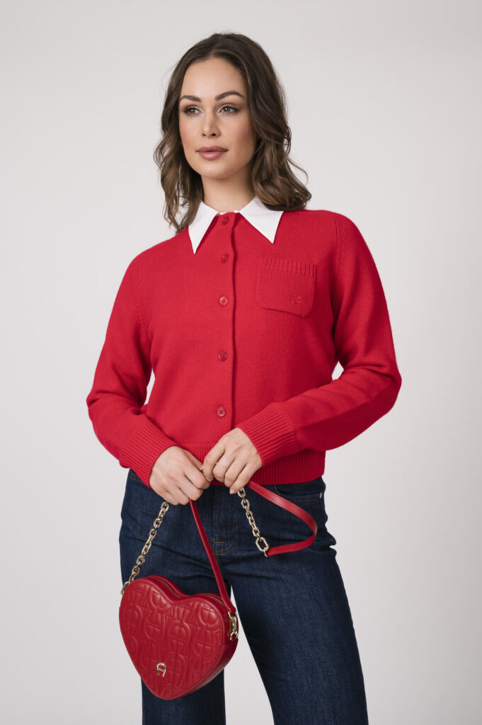 Model trägt einen roten Strickweste mit weißem Blusenkragen der Marke Dorothee Schumacher., eine dunkelblaue Jenas der Marke 7 for all mankind und eine herzförmige rote Tasche der Marke Aigner.