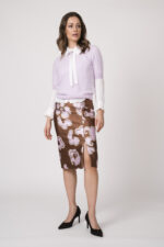 Model trägt eine weiße Bluse, eine Flieder farbigen Kurzarmpullover und einen beige rosa gemusterten Bleistiftrock der Marke Dorothee Schumacher.