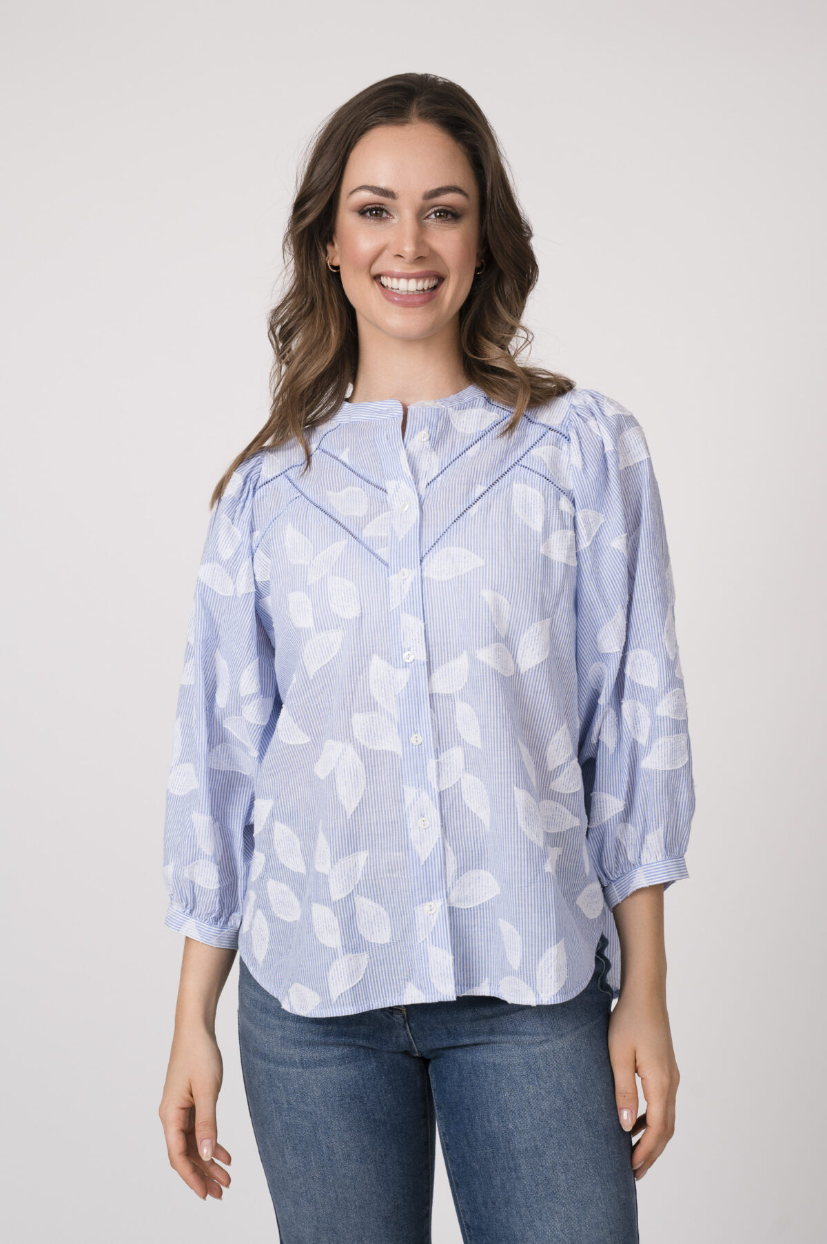 Model trägt eine hellblau-weiß gemusterte Bluse der Marke 0039 Italy und eine blaue Jeans der Marke Luisa Cerano.