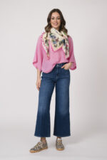 Model trägt einen feinen Cashmere-Kurzarmpullover der Marke Absolut Cashmere in Rosa, dazu einen passenden Schal der Marke Faliero Sarti und eine Jeans der Marke 7 for all mankind. Die Sneaker mit Leo Optik sind von Caval.