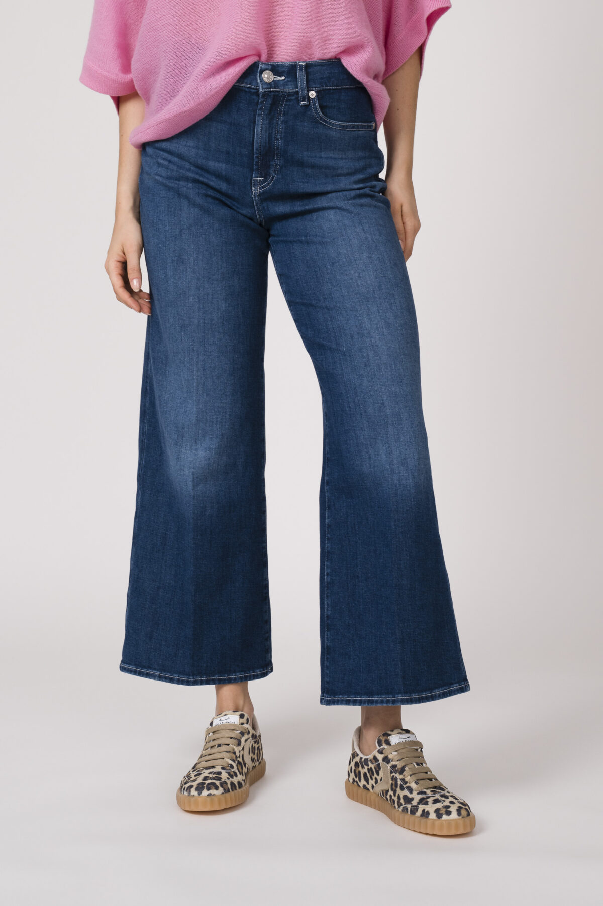 Model trägt einen feinen Cashmere-Kurzarmpullover der Marke Absolut Cashmere in Rosa, Jeans der Marke 7 for all mankind und Sneaker in Leo Optik der Marke Caval.