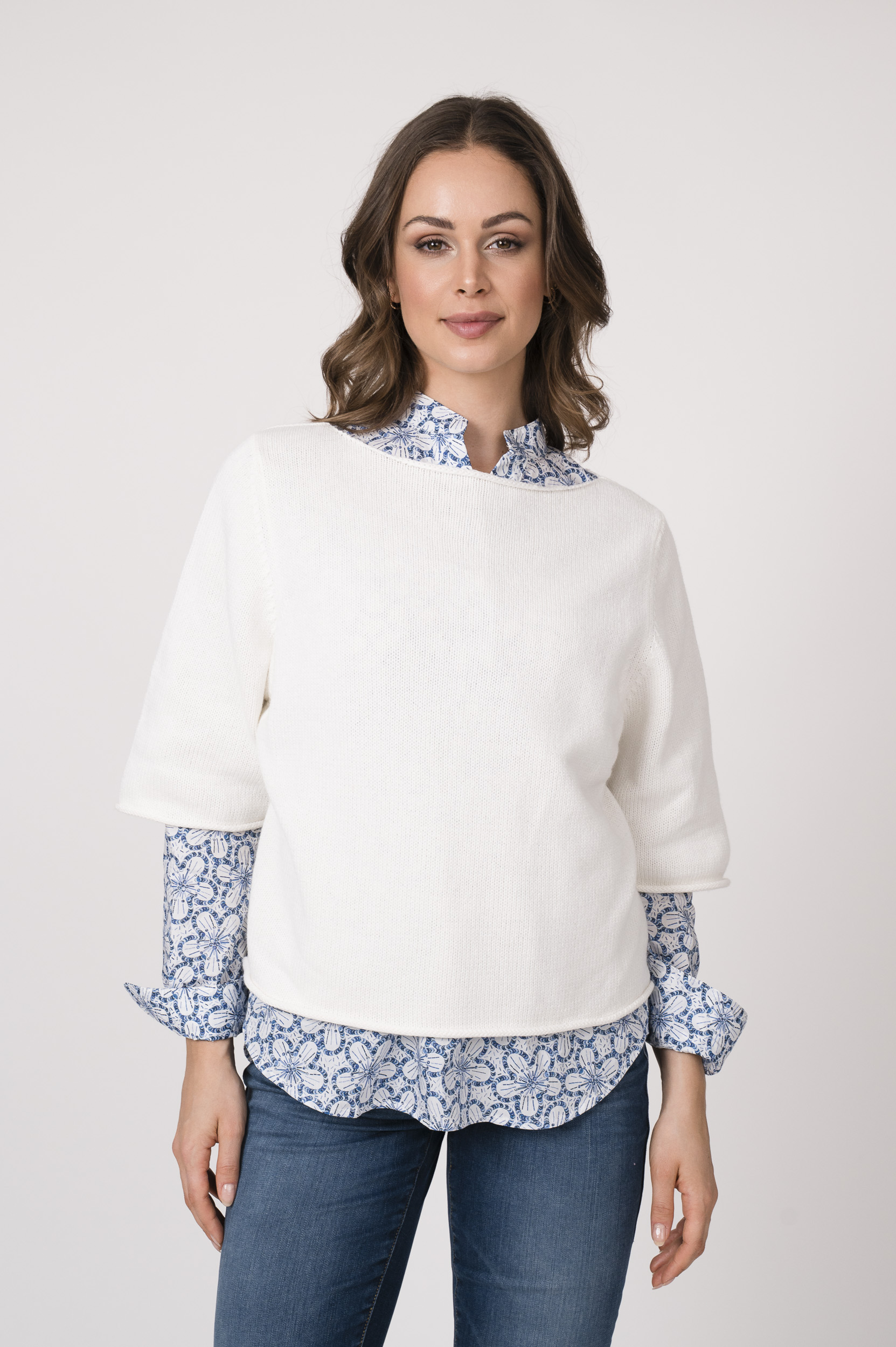 Model trägt einen weißen Kurzarmpullover der Marke Allude, die Bluse mit Blumenmuster ist von der Marke Rossana Diva.