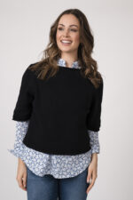 Model trägt einen schwarzen Kurzarmpullover der Marke Allude, die Bluse mit Blumenmuster ist von der Marke Rossana Diva