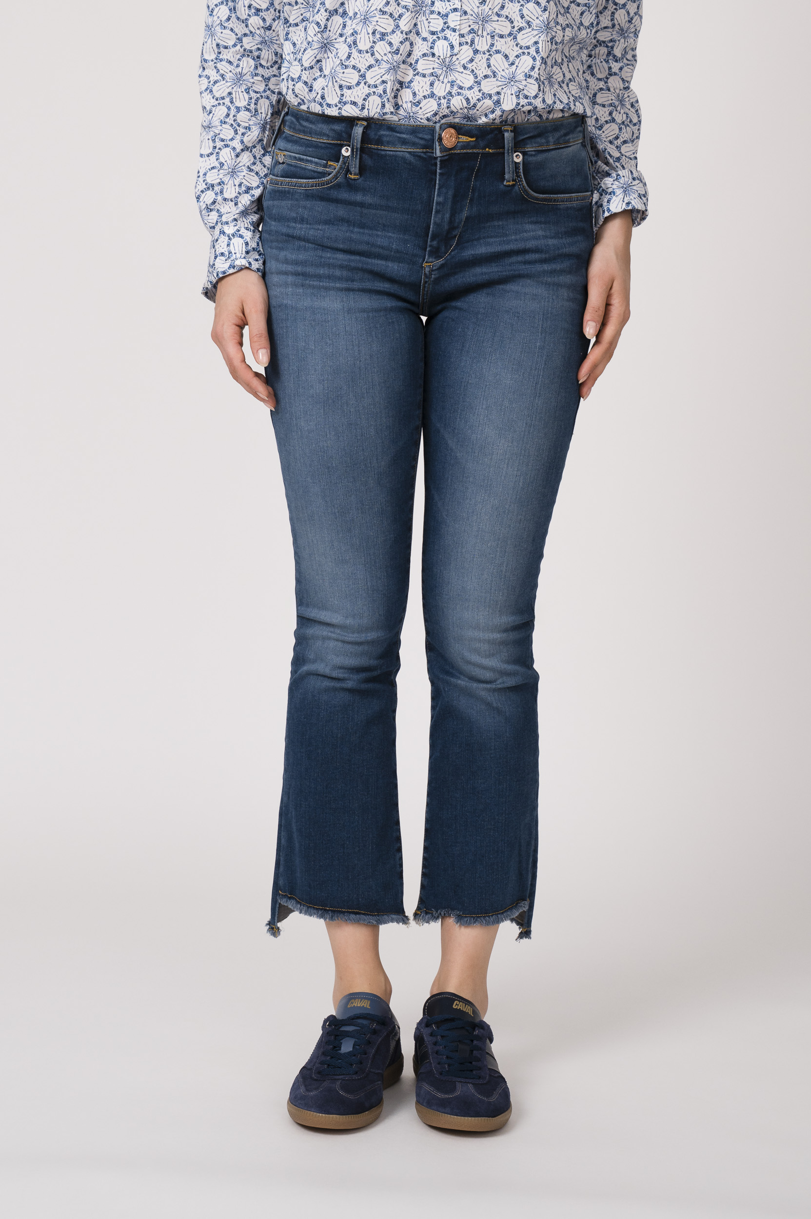 Model trägt eine Bluse mit Blumenmuster der Marke Rossana Diva, eine Jeans der Marke True Religion und blaue Sneaker der Marke Caval