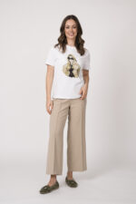 Model trägt ein weißes Shirt mit Zeichnung einer Frau der Marke Unartig und eine beige Hose der Marke Cambio.