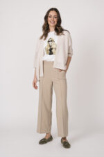 Model trägt eine sand-farbige Strickweste der Marke Hemisphere, ein weißes Shirt mit Zeichnung einer Frau der Marke Unartig und eine beige Hose der Marke Cambio.