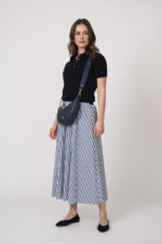 Model trägt einen marine-blauen Kurzarmpullover der Marke Allude und einen blau weiß gestreiften Rock der Marke JOOP sowie einer dunkelblauen Halbmondtasche der Marke Aigner.