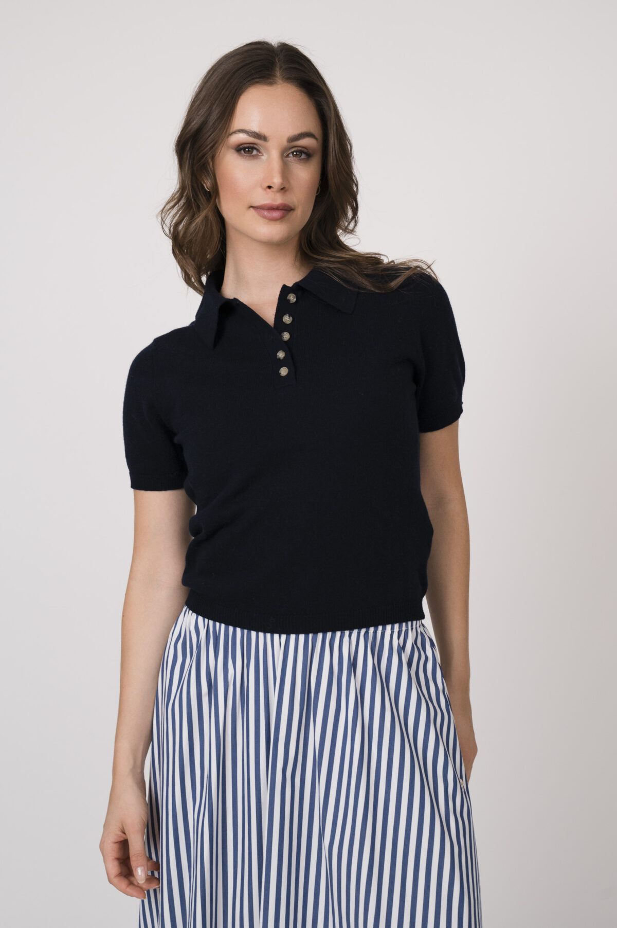 Model trägt einen marine-blauen Kurzarmpullover der Marke Allude und einen blau weiß gestreiften Rock der Marke JOOP.