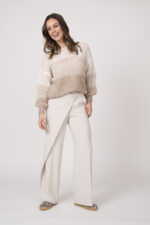 Model trägt einen hellen Strickpullover der Marke Michelle & Hoven und eine natur-farbige Stoffhose der Marke Cambio sowie Sneaker in Leo-Print der Marke Voile Blanche.