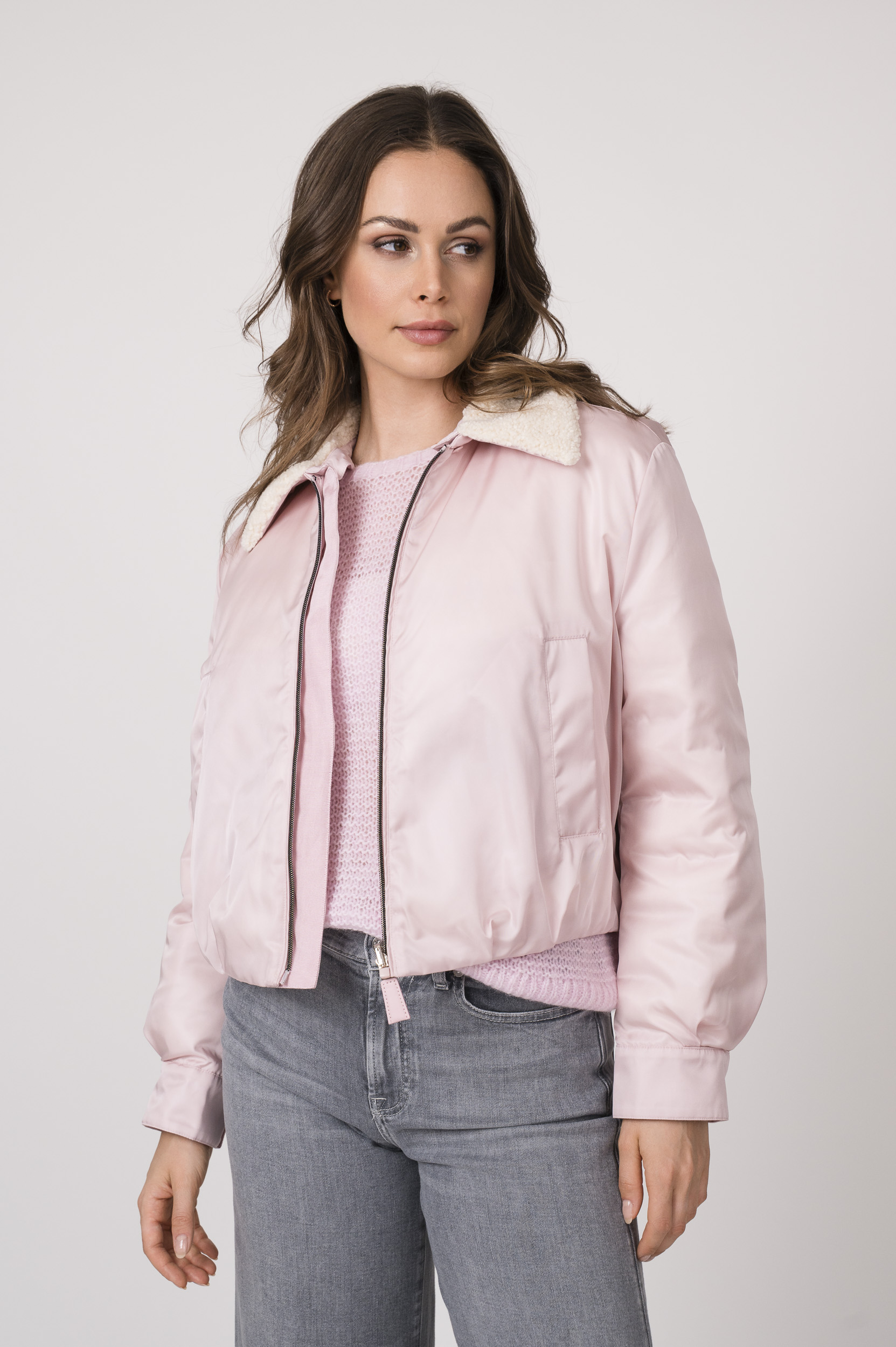 Model trägt eine rosa Daunen-Wendejacke der Marke Luisa Cerano, einen rosa Pullover der Marke Luisa Cerano und hellgraue Jeans der Marke 7 for all mankind.