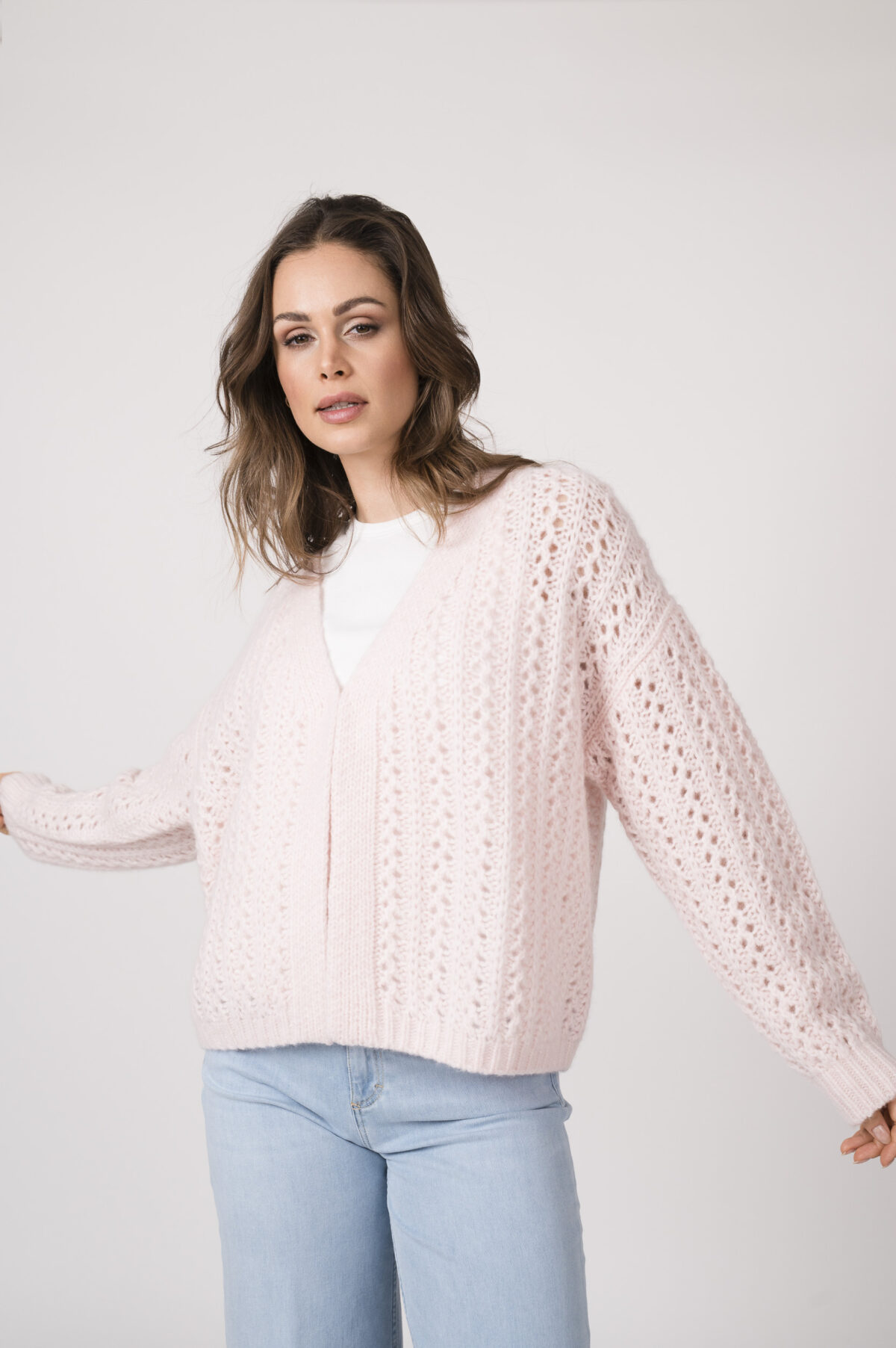 Model trägt eine rosé Strickweste der Marke Hemisphere, ein weißes Top der Marke Luisa Cerano und eine hellblaue Jeans der Marke Closed.
