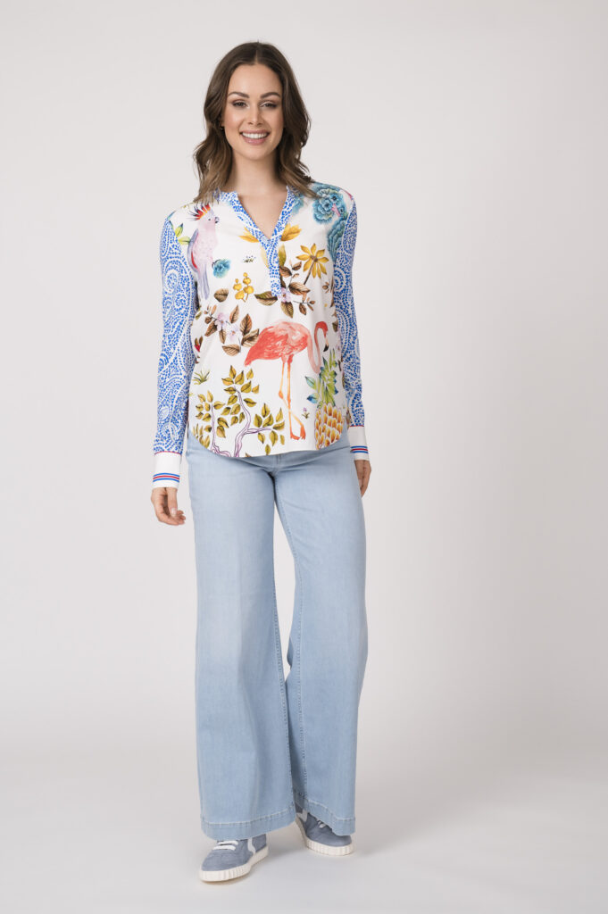 Model trägt eine bunte Bluse der Marke Herzens und eine hellblaue Jeans der Marke Closed sowie hellblaue Sneaker der Marke Voile Blanche.