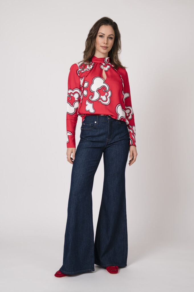 Model trägt eine rot weiß gemusterte Bluse der Marke Dorothee Schumacher und eine dunkel-blaue Jeans der Marke 7 for all mankind.