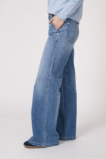 Model trägt einen Langarmpullover mit Rundhals der Marke Alliude in Blau. Dazu eine Jeans in Hellblau der Marke Cambio.