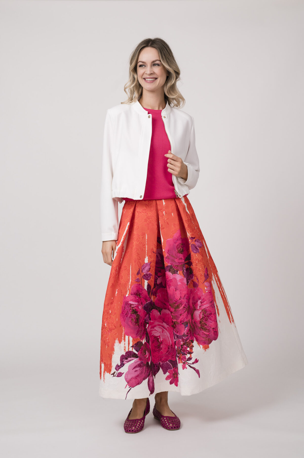 Model trägt eine weiße Blazerjacke von Marc Cain, ein pinkes Shirt von Kontatto und einen orange-pink-weißen Rock von Lunatica.