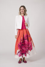 Model trägt eine weiße Blazerjacke von Marc Cain, ein pinkes Shirt von Kontatto und einen orange-pink-weißen Rock von Lunatica.