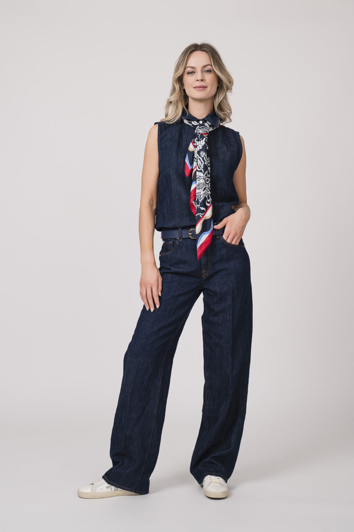 Model trägt eine dunkelblaue ärmellose Jeansbluse und Jeanshose der Marke 7 for all mankind und ein rot, weiß dunkelbalues Tuch von Joop! sowie einen dunkelblauen Gürtel von Aigner.