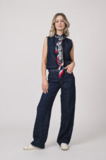 Model trägt eine dunkelblaue ärmellose Jeansbluse und Jeanshose der Marke 7 for all mankind und ein rot, weiß dunkelbalues Tuch von Joop! sowie einen dunkelblauen Gürtel von Aigner.