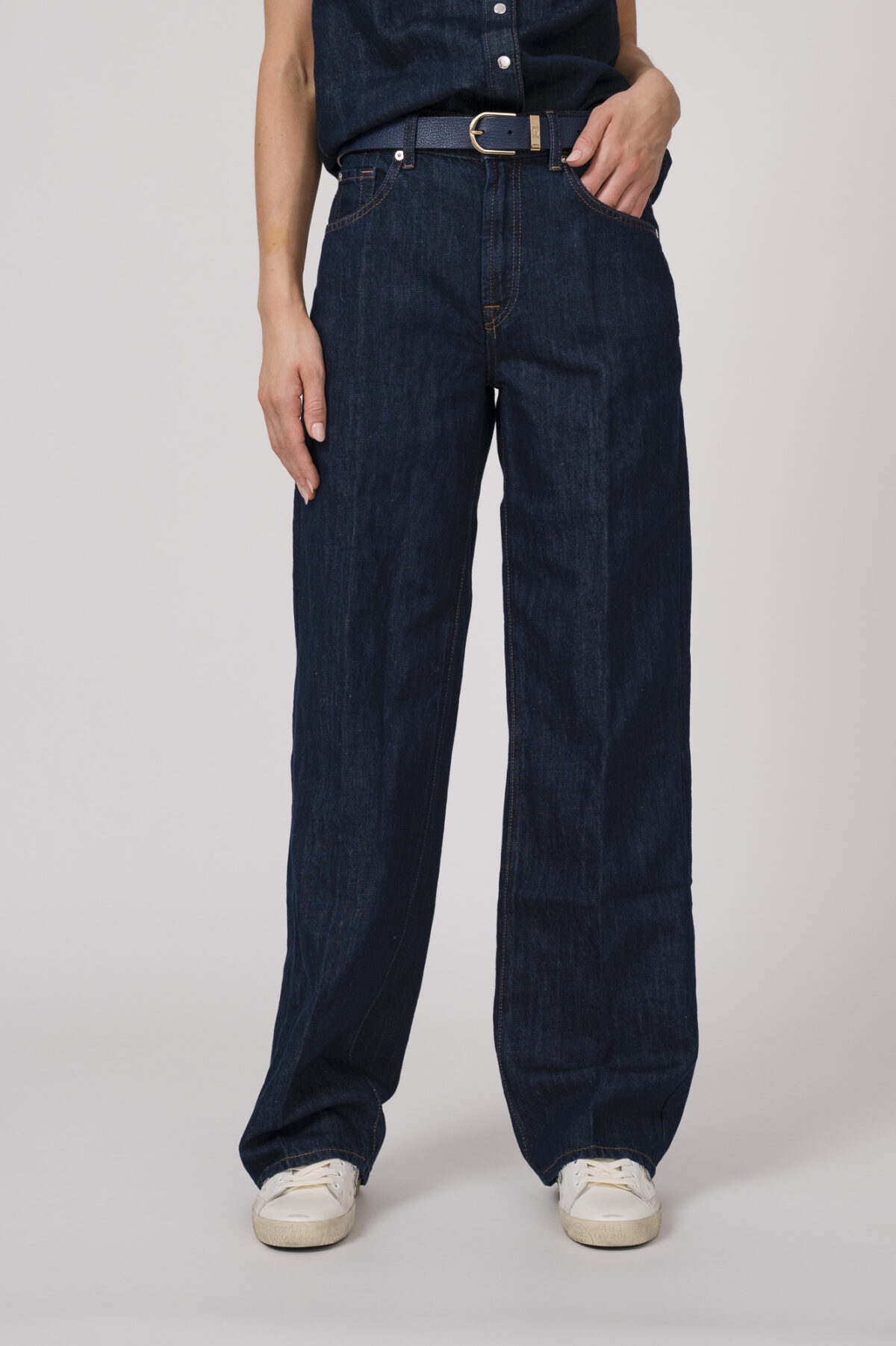 Model trägt eine dunkelblaue Jeanshose der Marke 7 for all mankind und einen dunkelblauen Gürtel von Aigner.