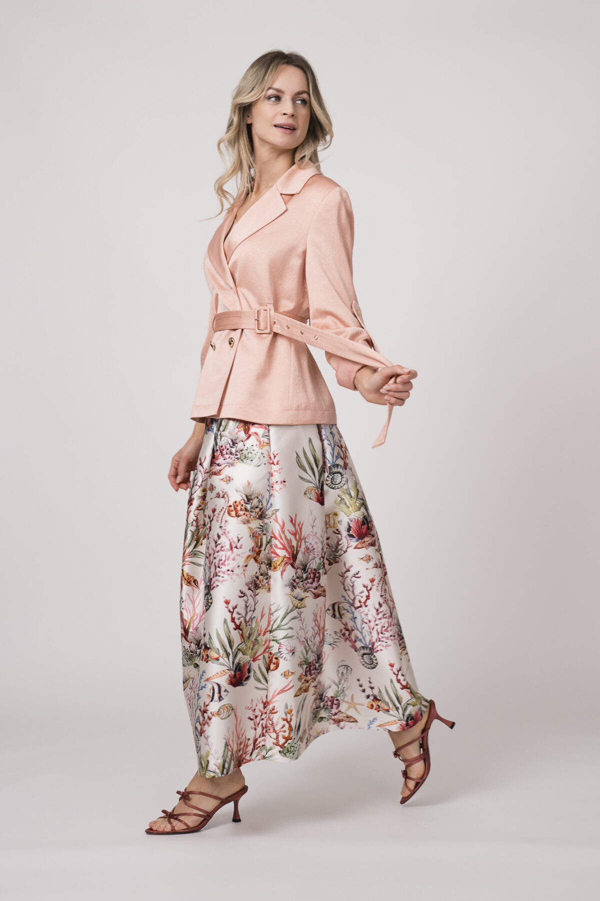 Model trägt einen pfirsich-farbigen Blazer von Marc Cain, ein natur-farbiges Top von Herzens und einen gemusterten Rock von Lunatica.