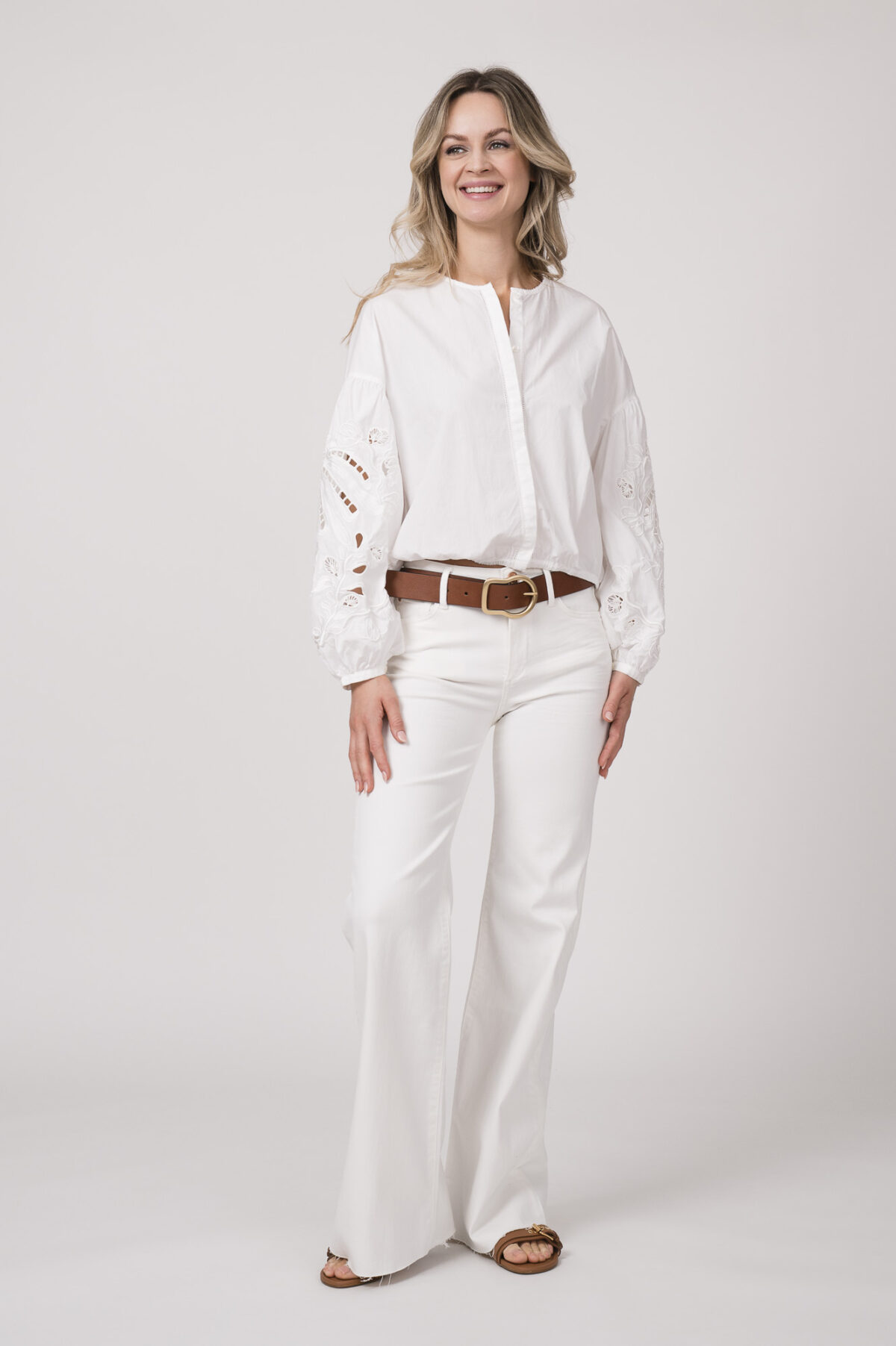 Model trägt eine weiße Bluse der Marke Dorothee Schumacher und eine weiße Jeans von True Religion. Der braue Gürtel ist von Dorothee Schumacher.