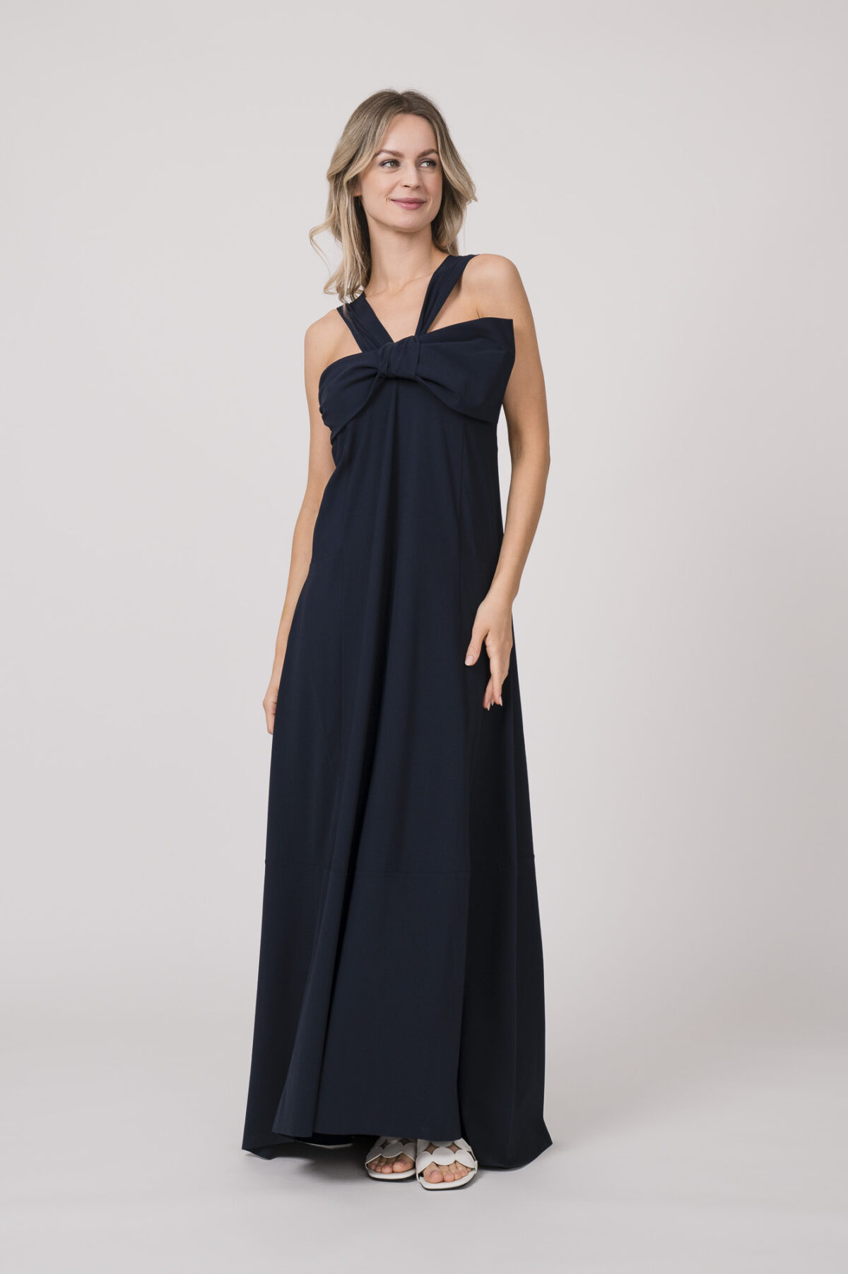 Model trägt ein marine-blaues Kleid mit Schleifendetail beim Dekolleté der Marke Dorothee Schumacher.