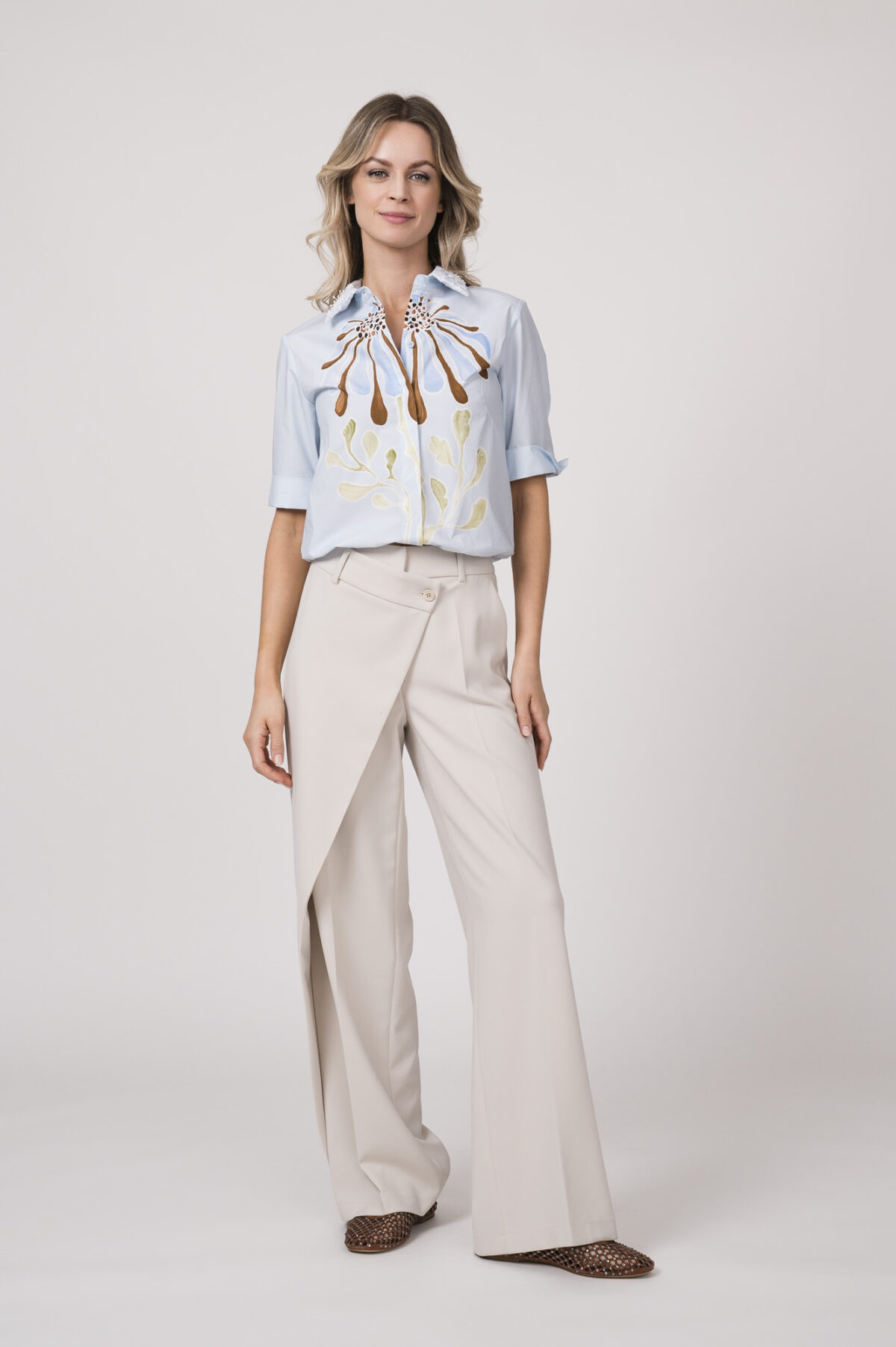 Model trägt eine hellblaue Bluse mit Blumenmuster der Marke Dorothee Schumacher und eine natur-weiße Hose der Marke Cambio.