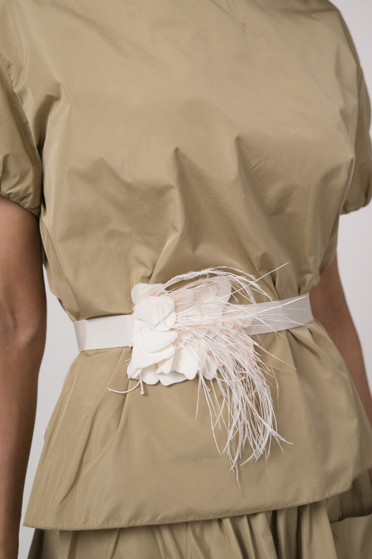 Model trägt einen beigen Rock, ein beiges Kurzarm-Oberteil und einen Federgürtel in weiß der Marke Susanne Bommer