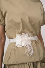 Model trägt einen beigen Rock, ein beiges Kurzarm-Oberteil und einen Federgürtel in weiß der Marke Susanne Bommer
